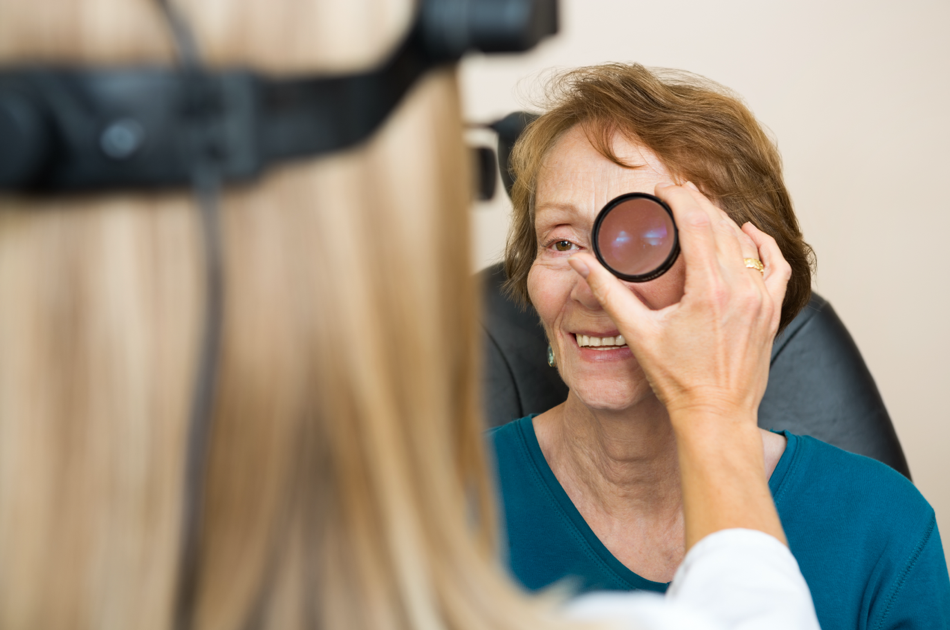 dryAMD.eu Professionista che indossa un oftalmoscopio montato sulla testa e tiene una lente manuale esaminando l'occhio di una paziente.