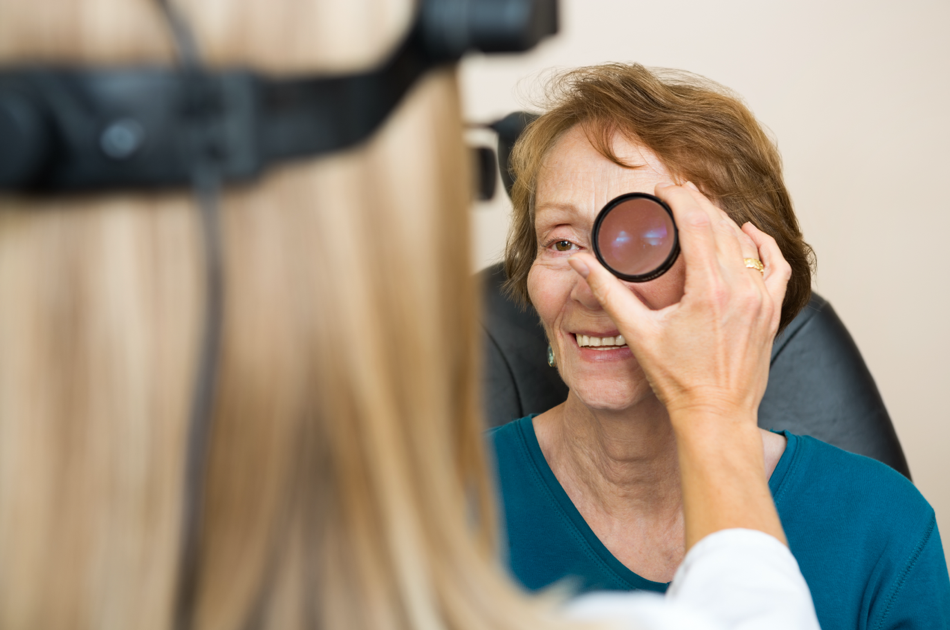 dryAMD.eu Praticien portant un ophtalmoscope monté sur la tête et tenant une lentille à main, examinant l'œil d'un patient.